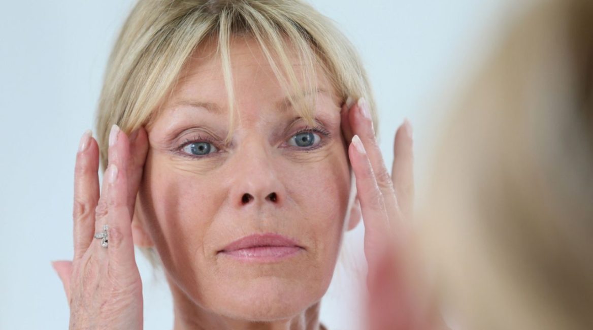 Femme mûre examinant sa peau dans un miroir, illustrant l'impact des traitements esthétiques tels que la mésothérapie et les injections d'acide hyaluronique sur le visage.
