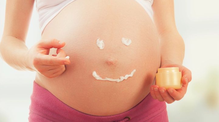 Femme enceinte appliquant une crème sur son ventre, avec un visage souriant dessiné en crème sur la peau, illustrant les soins esthétiques pendant la grossesse.