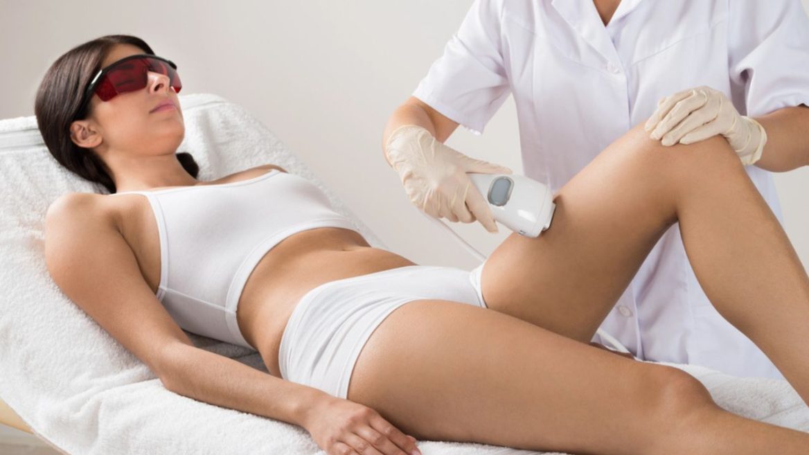 Femme allongée recevant une séance d'épilation laser sur les jambes par une praticienne en blouse, dans un cabinet esthétique.