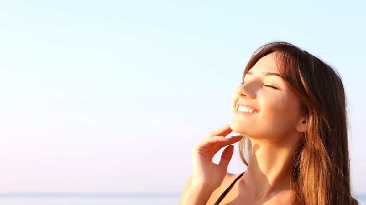 Jeune femme souriante profitant du soleil après un soin du visage, illustrant l'importance de la protection solaire après un peeling