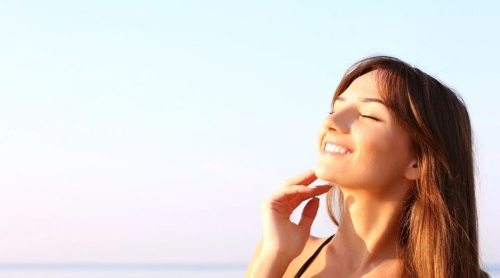 Jeune femme souriante profitant du soleil après un soin du visage, illustrant l'importance de la protection solaire après un peeling