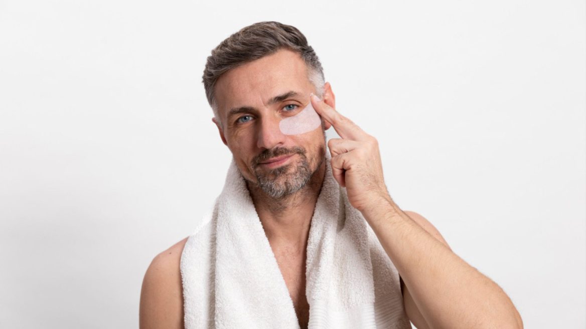 Homme appliquant un soin contour des yeux avec patch hydratant, illustrant une routine de soins de la peau masculine pour lutter contre les signes de fatigue.