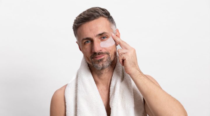 Homme appliquant un soin contour des yeux avec patch hydratant, illustrant une routine de soins de la peau masculine pour lutter contre les signes de fatigue.